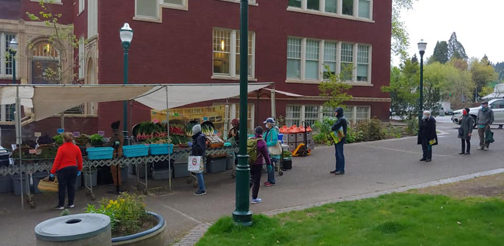 A few people buying goods at Portland Farmer’s Market