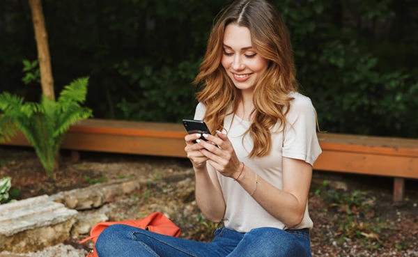 A blonde woman using the top Tulsa dating apps in a park