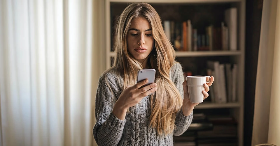 Blonde woman using free dating apps while drinking coffee