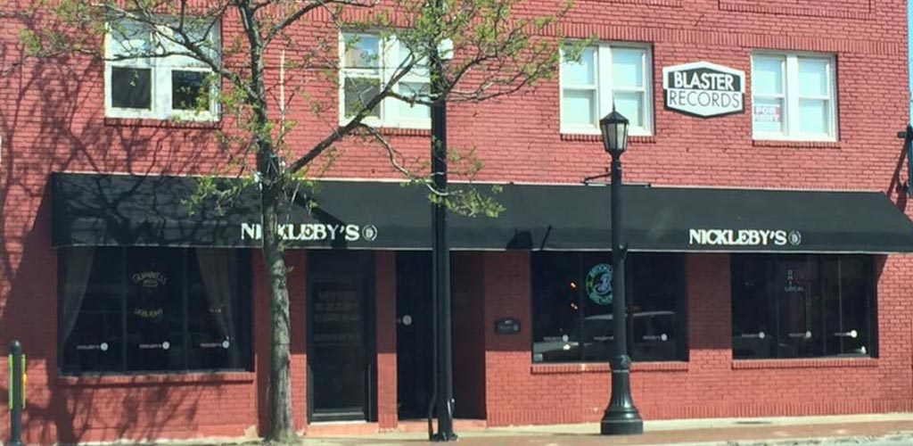 The redbrck exterior of Nickleby’s Roundbar & Kitchen with black outer awning that has Nickleby's written on it in white twice, spaced out