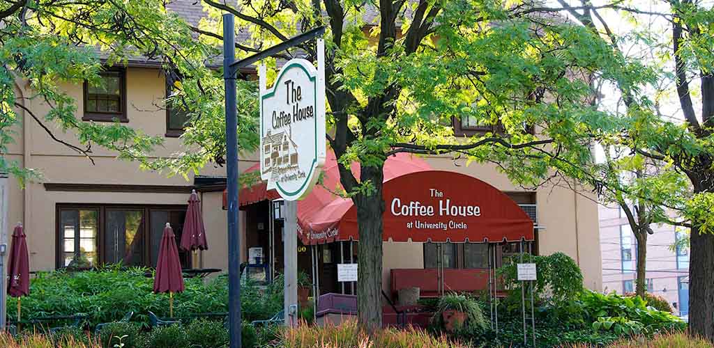 The Coffee House written in white on a long red awning extending from a tan-peach cafe