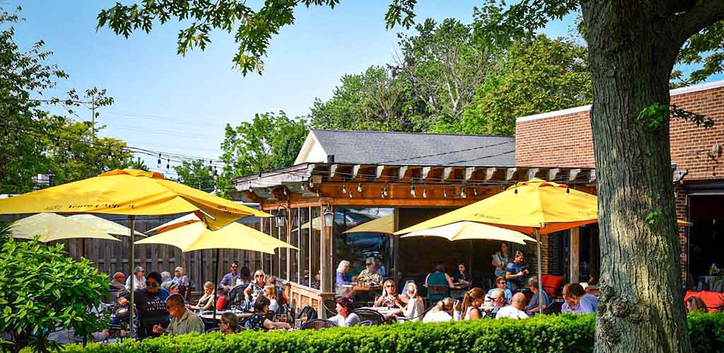 A sunny patio with yellow umbrellas at Wine Bar Rocky River with lots of young people having fun