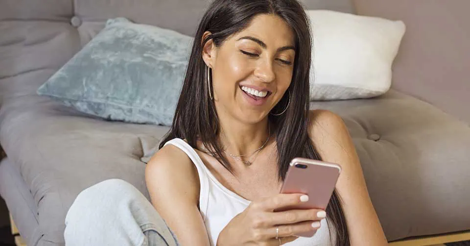 Beautiful young smiling woman sitting at home and using mobile