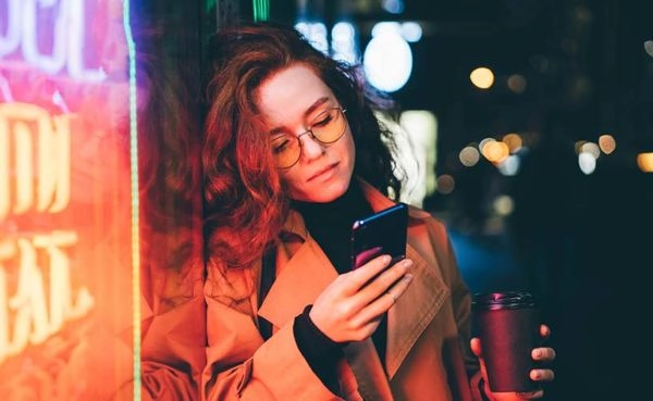 A woman using the top Spokane dating apps near a neon sign