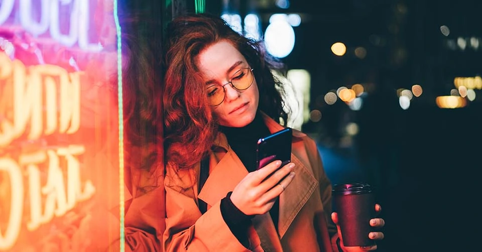 A woman using the top Spokane dating apps near a neon sign