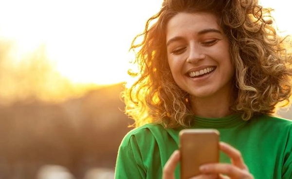 A woman with curly hair smiling while texting