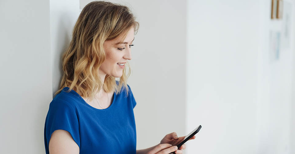 A blonde woman in a blue shirt using a South Dakota dating app at home